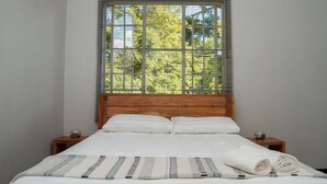 A neatly made bed with white linens and a patterned blanket, a wooden headboard, and a window with blinds.