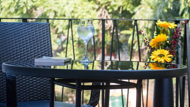 A balcony with a wicker chair, a table, a glass of water, and a vase with yellow flowers.