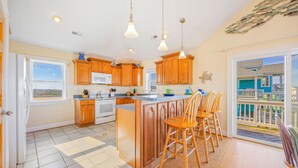 A kitchen with wooden cabinets, a white stove, and a large island with bar stools. - Oceanview Dog Friendly with Private Pool, Hot Tub, Elevator, Game Room, Theater (Rodanthe)