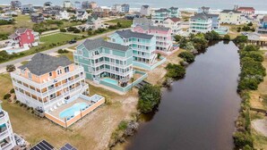 A coastal residential area with multi-story houses, a swimming pool, and a river. - Oceanview Dog Friendly with Private Pool, Hot Tub, Elevator, Game Room, Theater (Rodanthe)