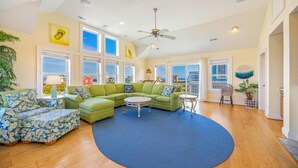 A spacious living room with a green sectional sofa, a round coffee table, and a blue rug. - Oceanview Dog Friendly with Private Pool, Hot Tub, Elevator, Game Room, Theater (Rodanthe)