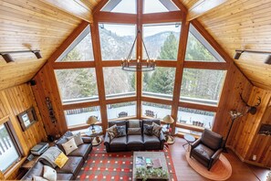 A wooden interior with a large window, a sofa, a coffee table, and a fireplace.