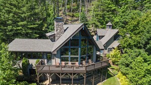 A large, multi-story cabin with a prominent deck and multiple windows, surrounded by dense forest. - Mountaineer Manor- views, hot tub, 3 acres fenced in yard, pool table (Sugar Grove)