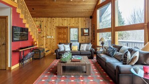 A wooden interior with a staircase, a sofa set, a coffee table, and large windows. - Mountaineer Manor- views, hot tub, 3 acres fenced in yard, pool table (Sugar Grove)