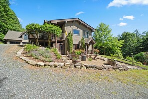 Una casa de dos pisos con un camino de piedra que lleva a la entrada, rodeada de vegetación y un cielo despejado.