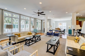 A spacious living room with large windows, a ceiling fan, and a variety of seating options including sofas and armchairs.