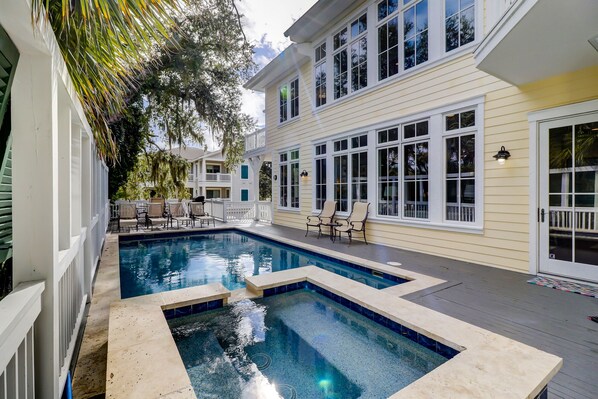 A swimming pool with a deck, surrounded by a white fence and trees.