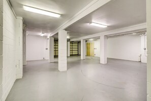 A spacious, empty parking garage with white walls and concrete floors, featuring multiple columns and doors.