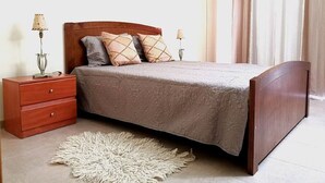 Quarto com cama de madeira, duas mesas de cabeceira com abajures, colcha estampada e tapete felpudo.
