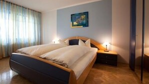 Una cama doble con estructura de madera, dos mesitas de noche con lámparas, un cuadro en la pared y una ventana con cortinas.