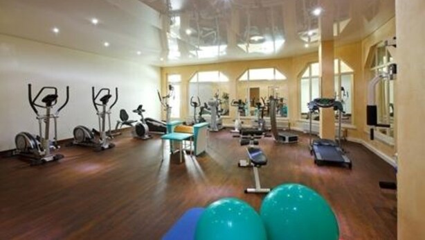 Un gimnasio espacioso con diversos equipos de ejercicio, como cintas de correr, bicicletas estáticas y pesas libres.