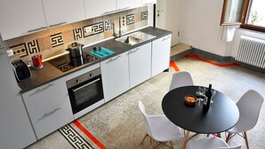 A modern kitchen with white cabinets, a black countertop, and a black dining table with white chairs. - - Piazza Arnolfo 1932- (Colle di Val d'Elsa)