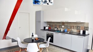 A modern kitchen with white cabinets, a black countertop, and a dining area with white chairs. - - Piazza Arnolfo 1932- (Colle di Val d'Elsa)