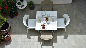 A patio table with white chairs, a white tablecloth, and a variety of potted plants. - - Piazza Arnolfo 1932- (Colle di Val d'Elsa)