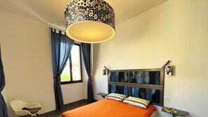A bedroom with a bed, a chair, a bedside table, and a window with curtains. - - Piazza Arnolfo 1932- (Colle di Val d'Elsa)
