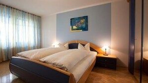 Una cama doble con estructura de madera, dos mesitas de noche con lámparas, un cuadro en la pared y una ventana con cortinas.