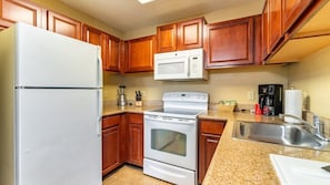 Compact kitchen with modern appliances, refrigerator, microwave, stove, and sink.