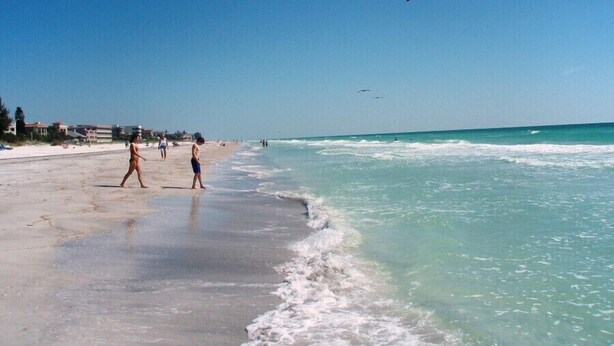 A beach with clear skies, calm waters, and a few people walking along the shore. -  Beachy Keen Cottage B!  Just Steps from Indian Rocks Beach! (Indian Rocks Beach)