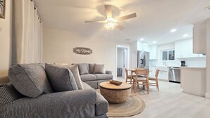 A modern living room with a grey sofa, a round wicker coffee table, and a ceiling fan. -  Beachy Keen Cottage B!  Just Steps from Indian Rocks Beach! (Indian Rocks Beach)