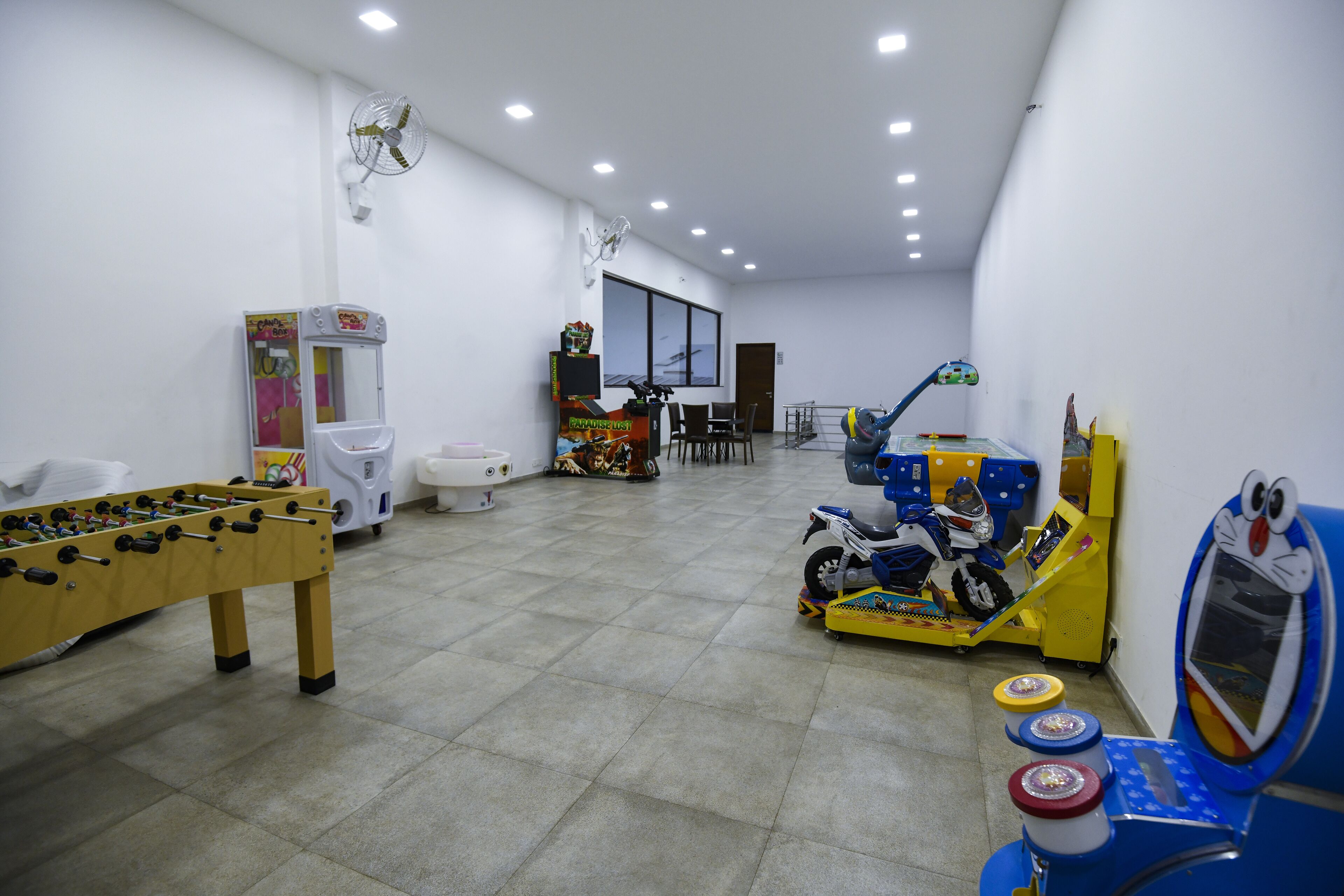 Una habitación con mesa de fútbol, una máquina de videojuegos de motocicletas y un pequeño área de juegos con un coche y un tren de juguete.