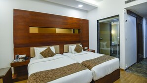 A hotel room with two beds, wooden headboard, bedside tables, and a glass door leading to a bathroom. - Spoorti Resort and Club (Bijapur)