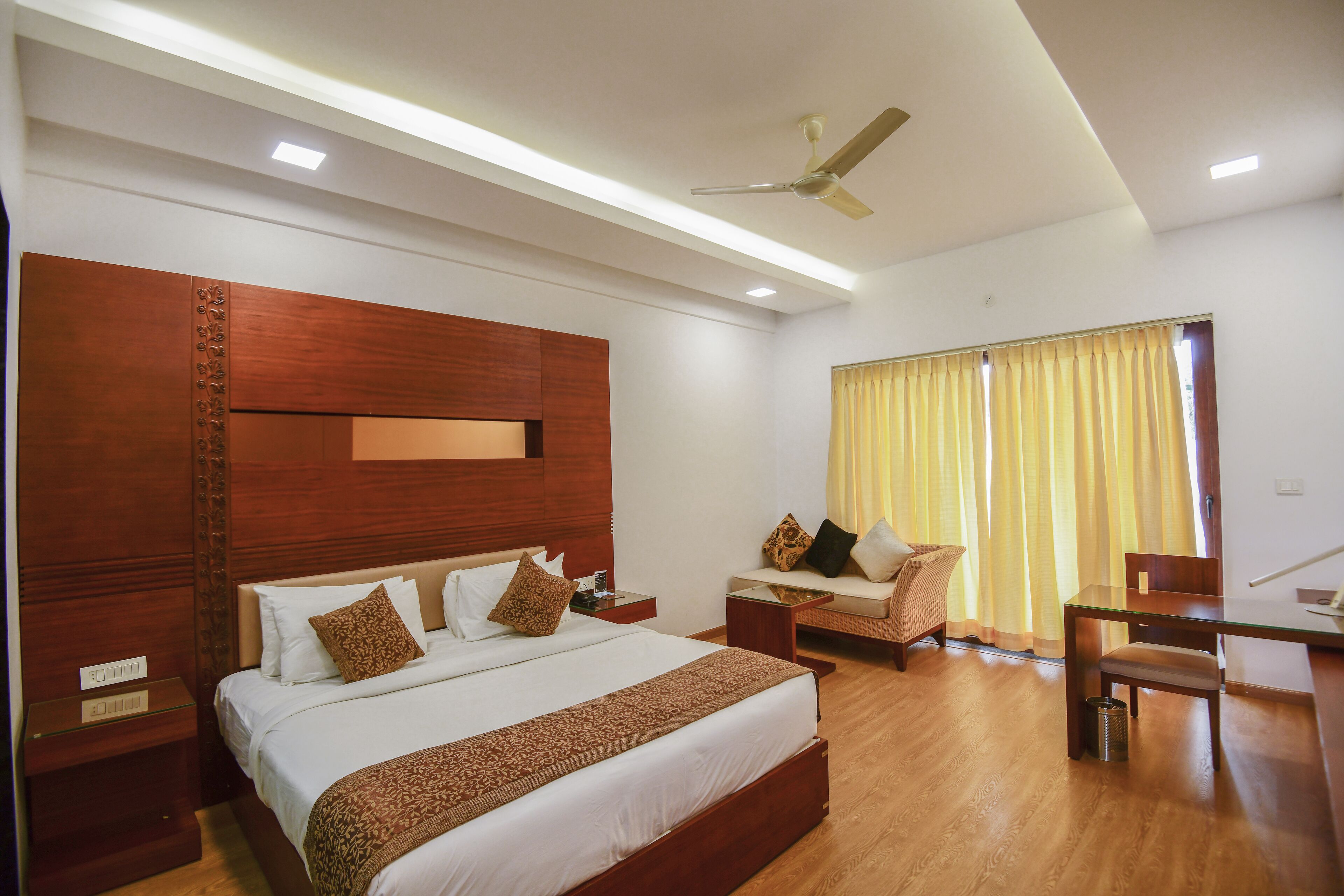 A modern hotel room with a large bed, a sofa, a desk, and a ceiling fan.