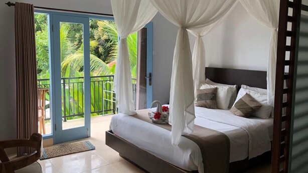 A bedroom with a bed, a chair, and a balcony with a view of greenery.