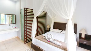 A bedroom with a canopy bed, a bedside table with a lamp, a nightstand, a mirror, and a bathroom with a sink and a towel rack.