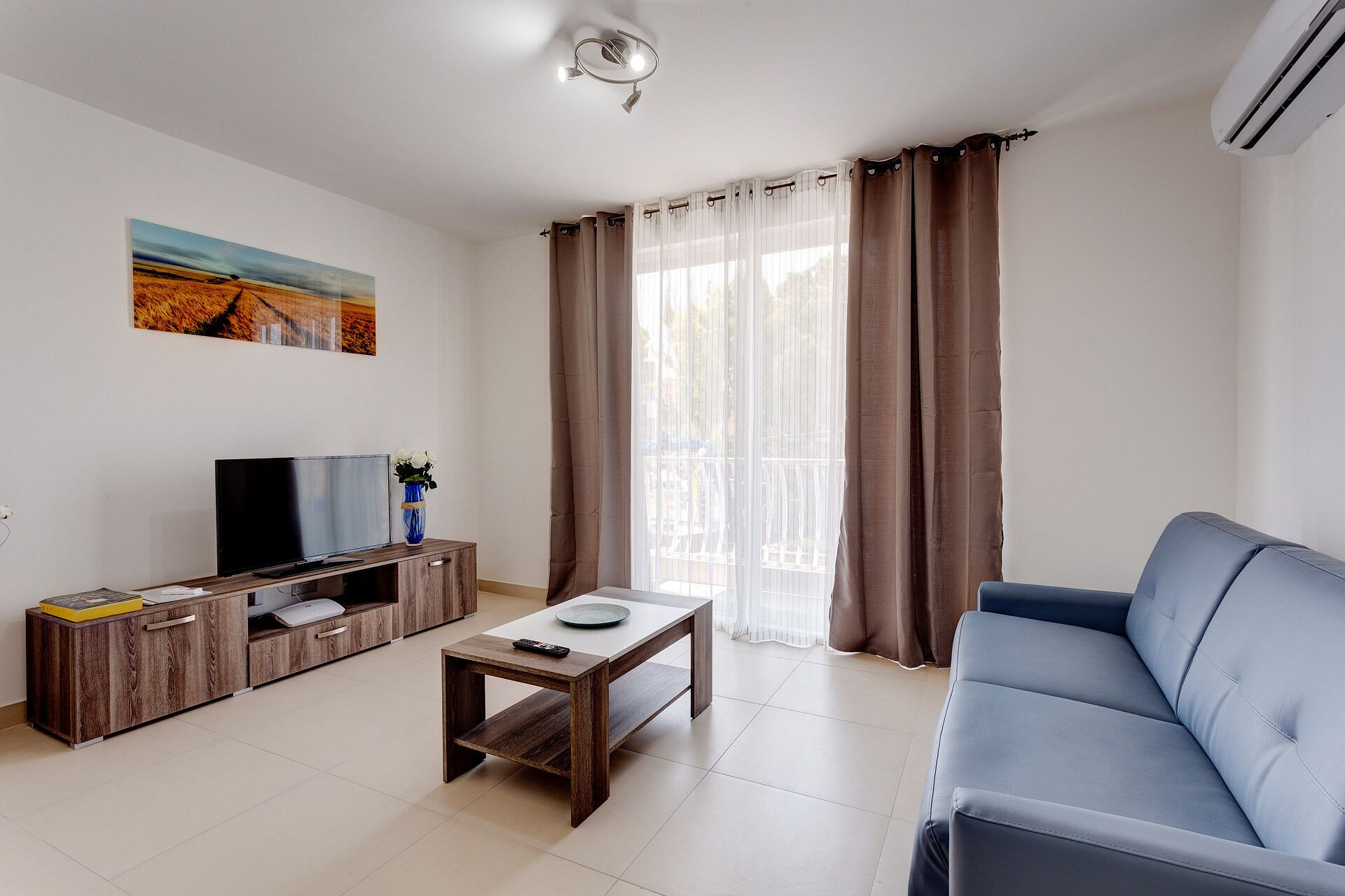 A living room with a TV, wooden cabinet, coffee table, and blue sofa.