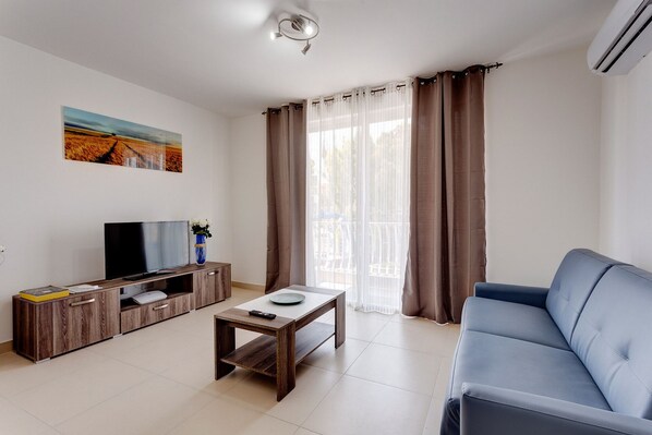 A living room with a TV, wooden cabinet, coffee table, and blue sofa. - Gorgeous 1BR Apartment close to Amenities (Msida)