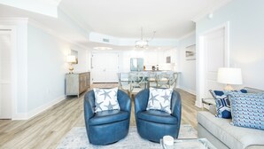 Una sala de estar moderna con un sofá, dos sillones y una mesa de centro. En el fondo, se aprecia un comedor con una mesa y sillas.
