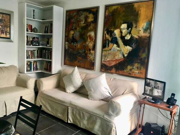 A living room with a beige sofa, a bookshelf, and two abstract paintings.