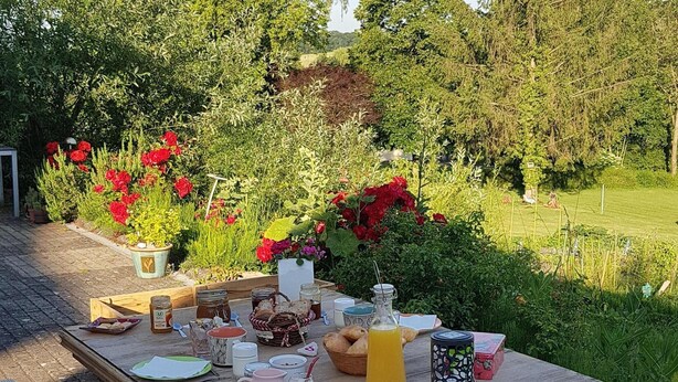 Een houten tuintafel gedekt met picknickspullen, omringd door groen en bloemen.