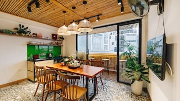 Un espace repas avec une table et des chaises en bois, un comptoir vert et une grande fenêtre donnant sur les bâtiments environnants.