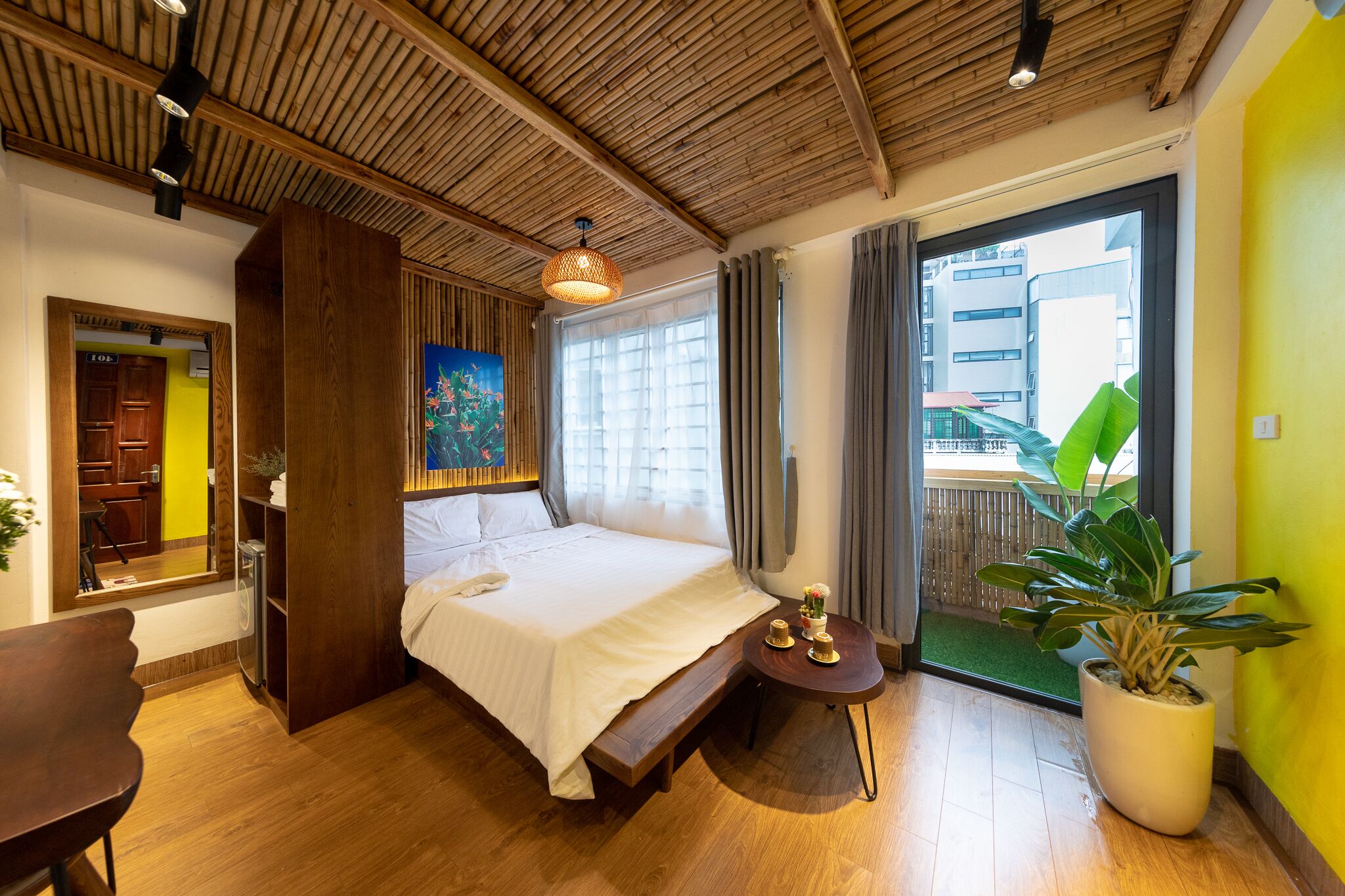 Une chambre moderne avec un plafond en bois, un grand lit, une petite table avec une plante et une vue sur un bâtiment à l’extérieur.