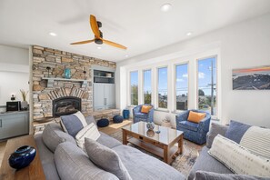 A spacious living room with a stone fireplace, large windows, and modern furniture.
