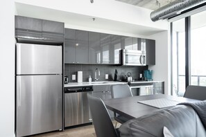 Enjoy meals at the dining table in this modern kitchen with stainless steel appliances and a large window.