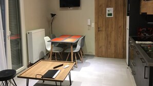 A compact kitchen with a dining table, chairs, a TV mounted on the wall, and a wooden door with a sign. - Sofie's Choice Mytilini (Lesvos)