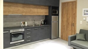 A modern kitchen with dark cabinetry, a built-in oven, a microwave, and a refrigerator. - Sofie's Choice Mytilini (Lesvos)