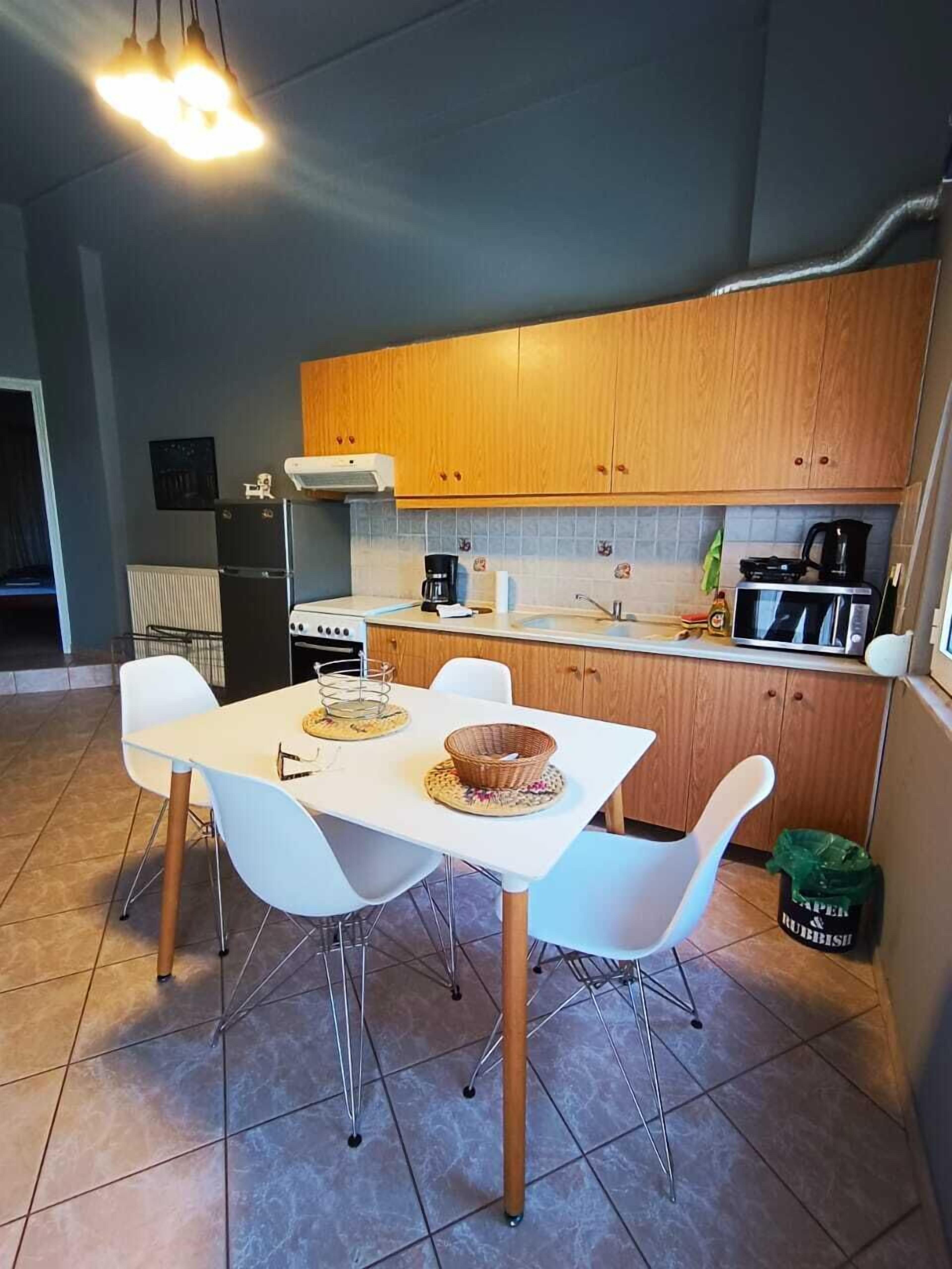 Una cocina moderna con armarios de madera, una mesa de comedor blanca con cuatro sillas y piso de baldosas.