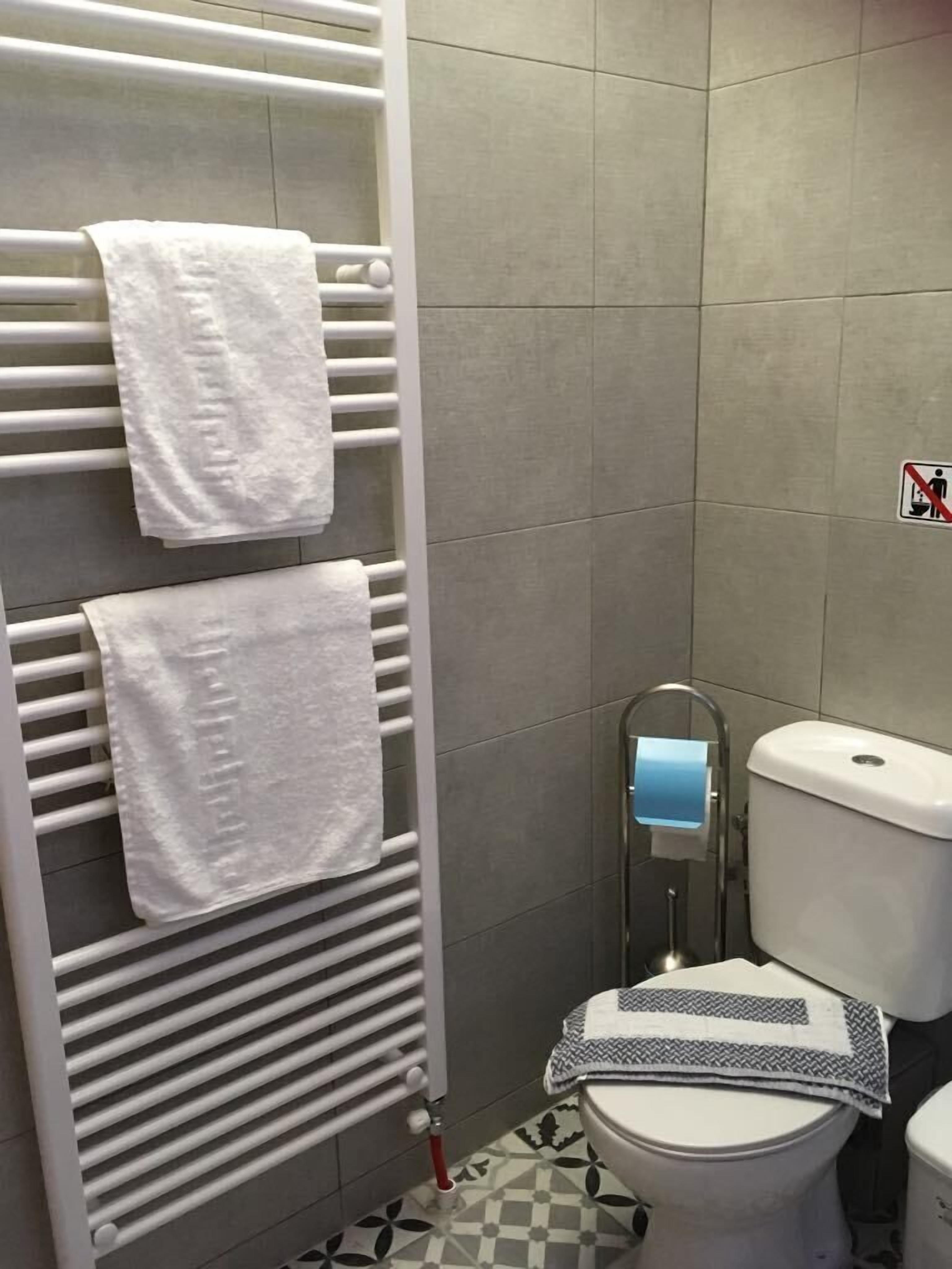 A bathroom with a toilet, a towel rack with two towels, a toilet paper holder, and a no digging sign on the wall.