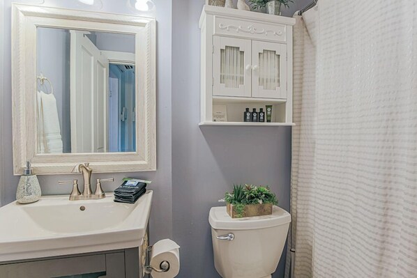 Un baño con lavamanos blanco, un espejo, un inodoro con jardinera y una cortina de ducha.