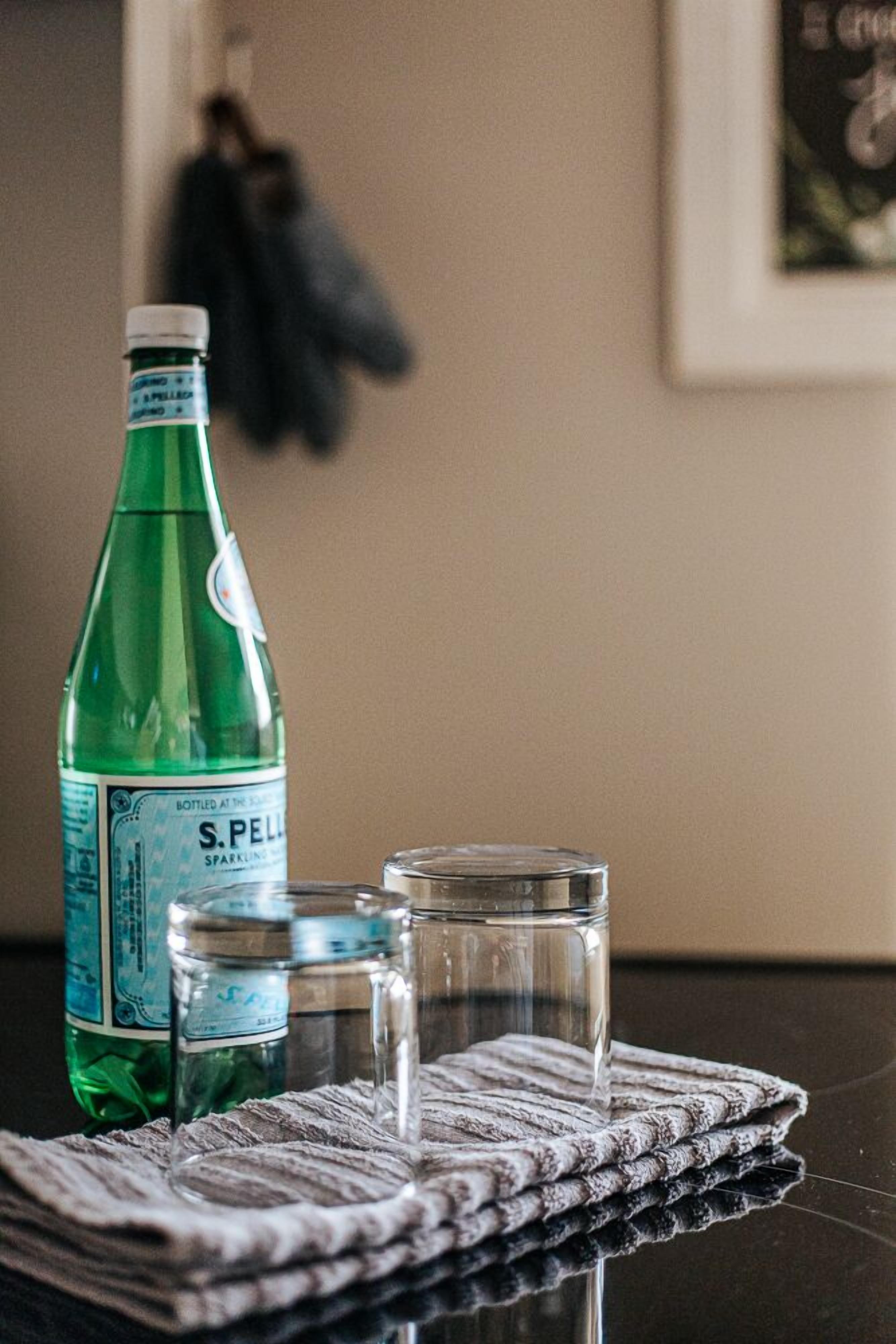 A bottle of S.Pelle sparkling water, two glasses, and a cloth on a table.