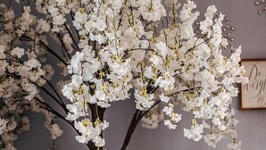 A room with a large artificial tree with white blossoms, a round glass table with a decorative sphere, and a framed sign on the wall. - The Serendipity Suite (Staunton)