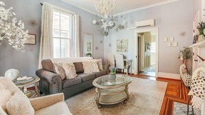 A living room with a grey sofa, a round glass coffee table, and a chandelier. - The Serendipity Suite (Staunton)