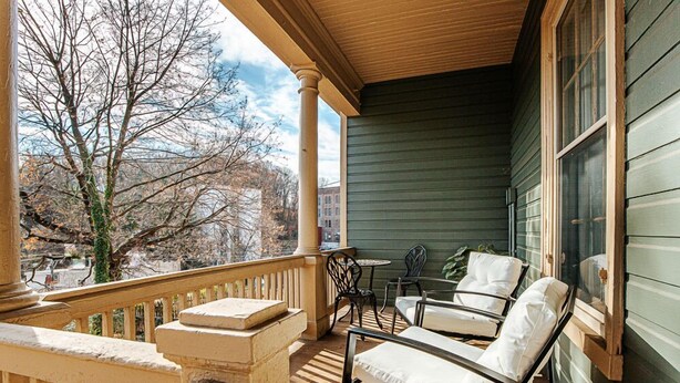 A covered porch with a wooden railing, a stone bench, and two chairs with cushions. - The Serendipity Suite (Staunton)
