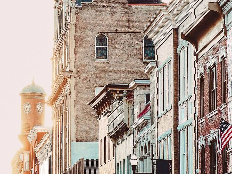 A historic downtown street with classic architecture, including a prominent clock tower and a building with a sign for Shenandoah Pizza.