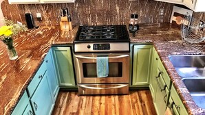 A kitchen with a stainless steel stove, oven, and microwave. There are green cabinets and a granite countertop. - Carbondale Townhome with A/C, WiFi, and Backyard (Carbondale)