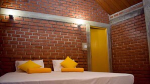 A room with a brick wall, a bed with white bedding and yellow pillows, and a yellow door. - Laana Villa (Negombo)