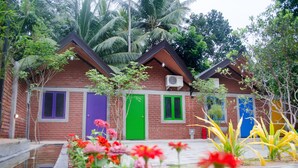 A two-story brick building with a green door and purple windows, surrounded by tropical vegetation and a small water feature. - Laana Villa (Negombo)